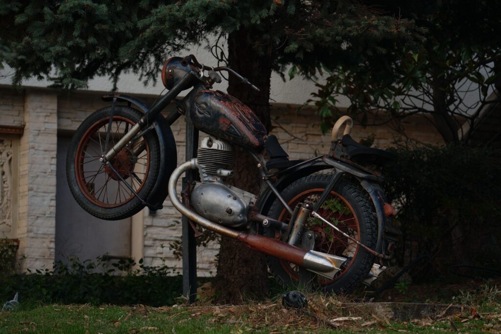 An old, rusted motorcycle displayed outdoors against a tree, adds vintage charm.